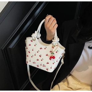 Détail du sac seau à imprimé cerise blanc avec poignée nouée et breloque cerise