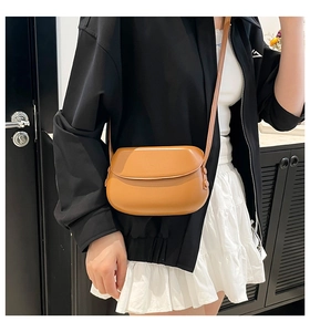 Close-up of a tan synthetic leather saddle bag worn cross-body on a model for daily use
