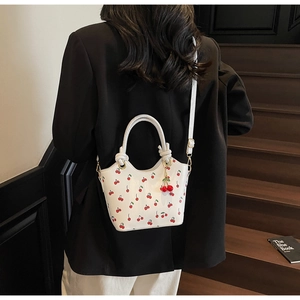 Détail d'un sac seau blanc à imprimé cerise avec poignée à nœud et pendentif cerise