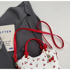 Détail d'un sac à main blanc avec imprimés cerises rouges, poignées et breloque dorée