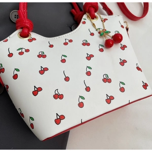 Détail du sac seau à imprimé cerise avec poignées rouges et pendentif cerise