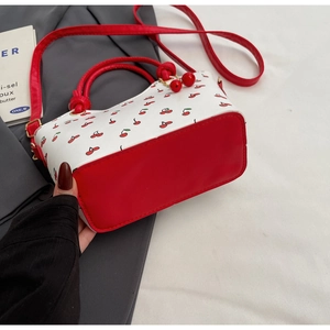 Détail du sac à main imprimé cerise avec poignées en cuir rouge et charm cerise en relief