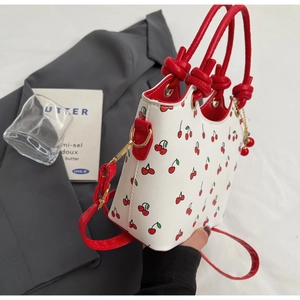 Détail latéral du sac à main en similicuir blanc avec imprimés cerises et boucles dorées