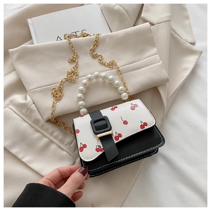 Detail of elegant cherry print handbag with large pearl handle and gold chain strap