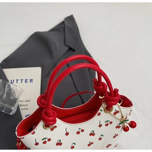 Détail du sac à main blanc à motif cerises avec anses rouges et pendentif cerise