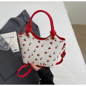 Détail du sac seau à motif cerise avec poignées rouges et finitions de bords ondulés