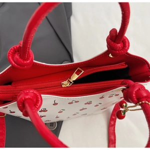 Détail du sac à main imprimé cerises avec poignée à nœud rouge et pendentif cerise chic