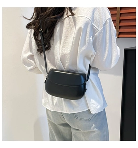 Modern black leather saddle bag with adjustable strap shown on model over white shirt