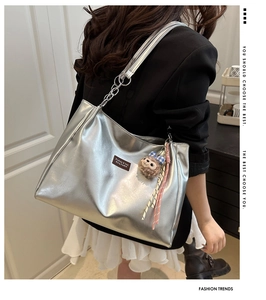 Silver metallic tote bag with chain strap and plush pendant detail on model