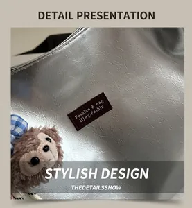 Close-up of silver glossy tote bag with leather logo patch and brown plush bear charm