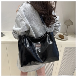 Glossy black tote bag with silver chain strap shown from a side view on a model's shoulder