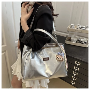 Detail of silver metallic tote bag with plush charm and brand label on shoulder strap