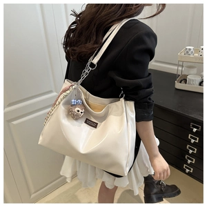 Detail of a large cream leather tote bag with silver chain strap and plush pendant