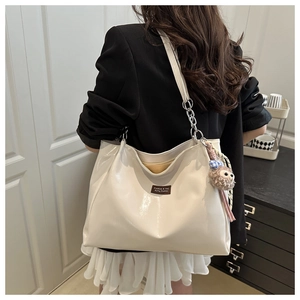 Close-up of cream glossy tote bag with metal chain strap and cute bear charm detail