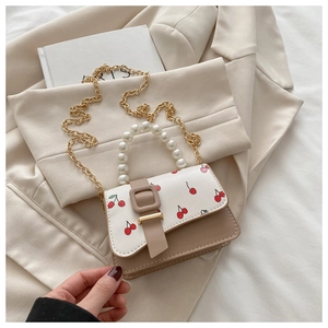 Detail of mini cherry print crossbody bag with pearl handle and golden chain strap