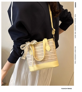 Detail of straw bucket bag with yellow leather trim and elegant lace bow decoration