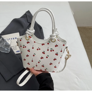 Détail du sac seau à imprimé cerise avec bords ondulés et boucles métalliques dorées