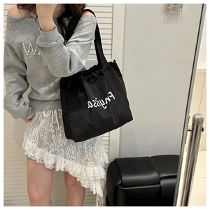 Close-up of black drawstring canvas bucket bag with white printed letters on casual outfit