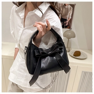 Détail d'un sac à main noir brillant avec nœud oversize et bandoulière chaîne