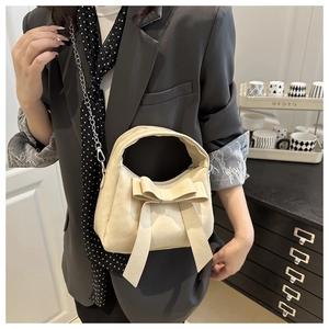 Détail du sac beige avec grand nœud et bandoulière chaîne porté par un mannequin