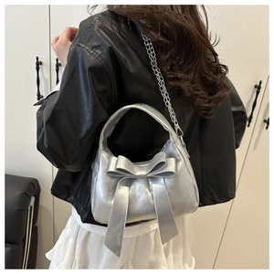 Détail d'un sac à main argenté métallisé avec grand nœud et bandoulière chaîne sur modèle