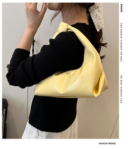 Detail of yellow glossy leather hobo bag with stylish pleated design on a model