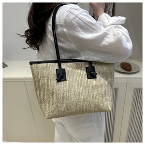 Detail of straw tote bag with black leather straps and knot accents on white linen outfit
