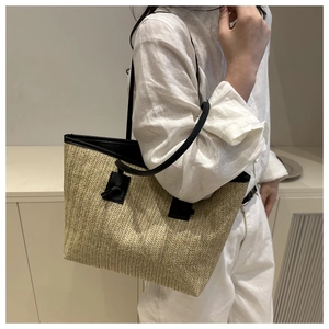 Detail of woven straw tote bag featuring contrast black leather shoulder straps and texture