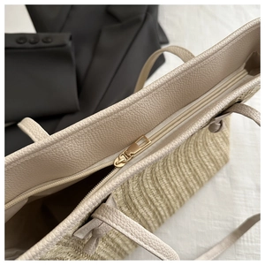 Close-up of the smooth beige leather trim and golden zipper on the woven straw tote bag