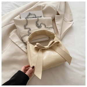 Gros plan du sac beige avec grand nœud décoratif et bandoulière en chaîne argentée