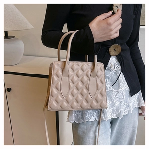 Detail of a beige quilted leather crossbody bag with top handles shown in hand