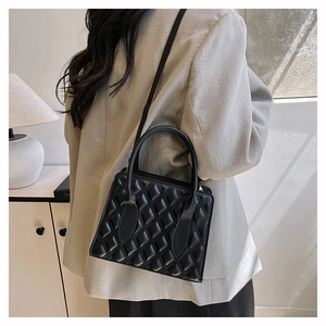Close-up of black quilted box bag featuring embossed texture and top handles