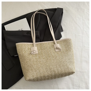 Detail of beige straw tote bag with knotted handles on textured background