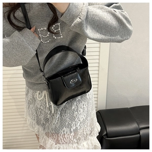 Glossy black PU leather crossbody bag with silver oval metal logo shown on model