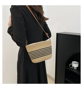 Close-up of woven straw tote bag featuring black stripes and brown leather strap details