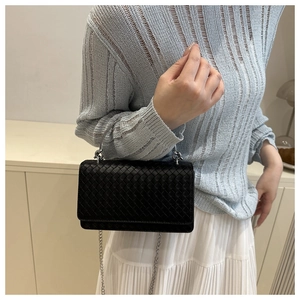 Close-up of black woven leather handbag with silver ring handle and chain strap detail