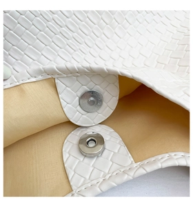 Close-up of the silver magnetic closure and woven leather texture on a white tote bag