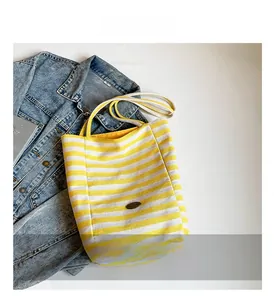 Detailed view of yellow striped canvas tote bag on denim jacket with textured fabric handles