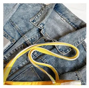 Detail of yellow canvas tote bag with contrast woven strap against denim background