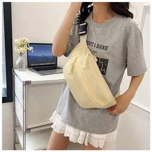 Detailed view of beige canvas crossbody bag with woven zipper pull on model