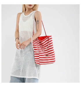 Detail of red and white striped canvas tote bag with metal logo and thin shoulder strap