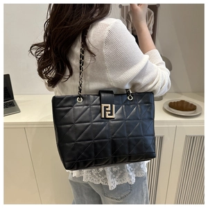 Close-up of quilted black leather tote featuring gold geometric clasp and chain strap