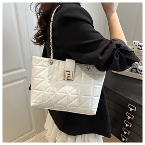 Detail of white quilted tote bag with gold metal logo and classic chain strap worn by a model