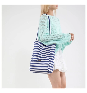 Close-up of blue striped canvas tote bag featuring an oval metal logo and slim strap