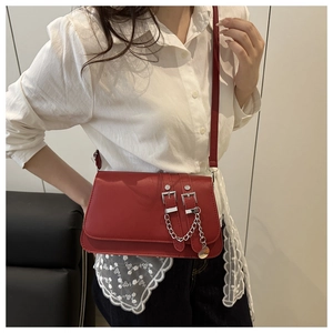 Detail of red crossbody bag featuring dual belt buckles and silver chain on white lace shirt