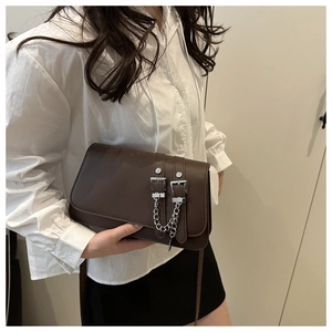 Detail of dark brown leather crossbody bag with buckle straps and silver chain