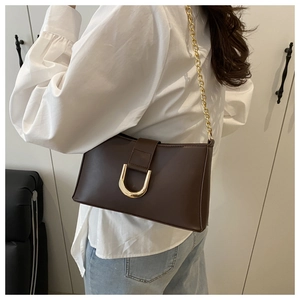 Detail of dark brown underarm bag with gold U-shaped buckle and metal chain strap
