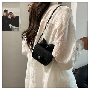 Detail of black quilted crossbody bag featuring a bow and silver flower magnetic clasp