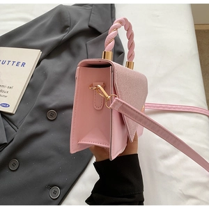 Pink handbag with braided handle and gold metal hardware on a white bed sheet