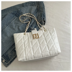 Detail of white quilted tote bag featuring gold-tone hardware and woven chain strap